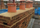 A chimney stack that has been neatly mended with fresh mortar (pointing) and new red clay bungs on top.