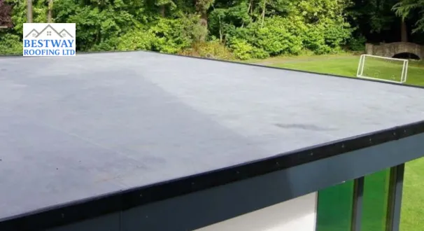 A smooth, grey EPDM rubber flat roof installed on a modern building, featuring clean black trim edges with a lush green forest and lawn in the background.