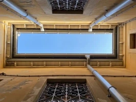 Extreme low-angle view of a narrow building alley showing newly installed grey UPVC fascias and guttering, with clean downpipes and preserved wrought iron window grille. Perfect example of local guttering repairs in Chelmsford.