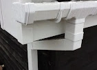 A close-up of brand new, bright white plastic guttering and downpipes fitted to the corner of a house.