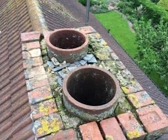 An old, crumbling chimney top covered in moss and bits of broken slate, showing it needs a proper bit of work.