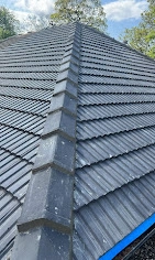 A professional Roofers Chelmsford finished roof with dark grey tiles and a very tidy, straight ridge line running down the corner.