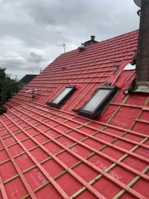 Close-up of a residential roof undergoing repair or re-roofing, showing red Marley breathable underlay membrane, freshly installed timber tiling battens, and two integrated Velux skylight windows.