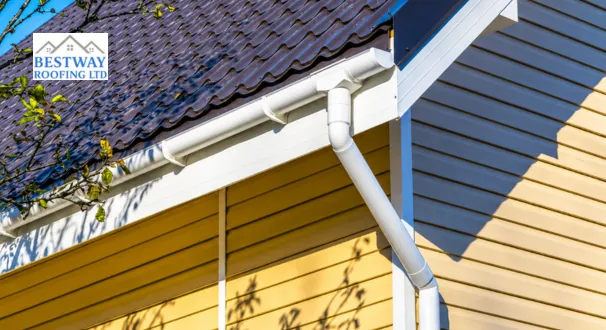 White uPVC gutter and vertical downpipe installed on a house with a brown metal roof. The additional Gutter Replacement Cost.
