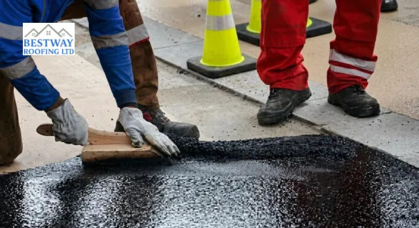 Professional operatives spreading a hot mastic asphalt waterproofing layer on a flat surface using a traditional wooden float.
