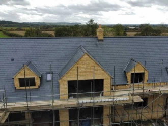 Aerial view of a newly installed slate tile roof on a luxury home under construction with scaffolding in Chelmsford.